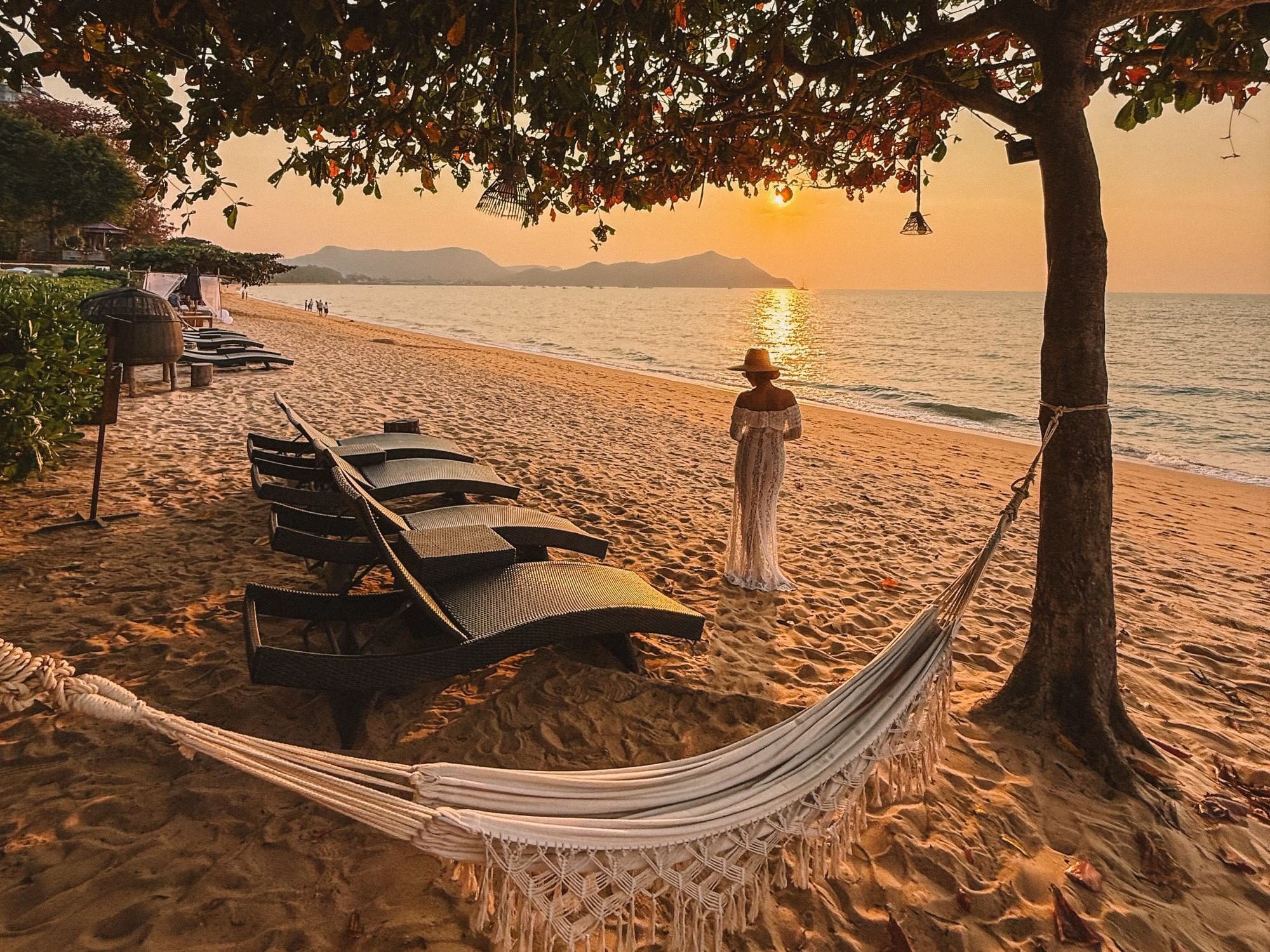 Golden hour beach scene with a hammock and sun loungers and a woman watching the ocean sunset at U Pattaya