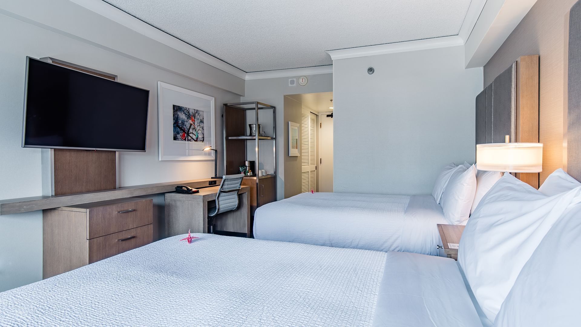 A hotel room with two double beds, a desk, TV, and lamp.