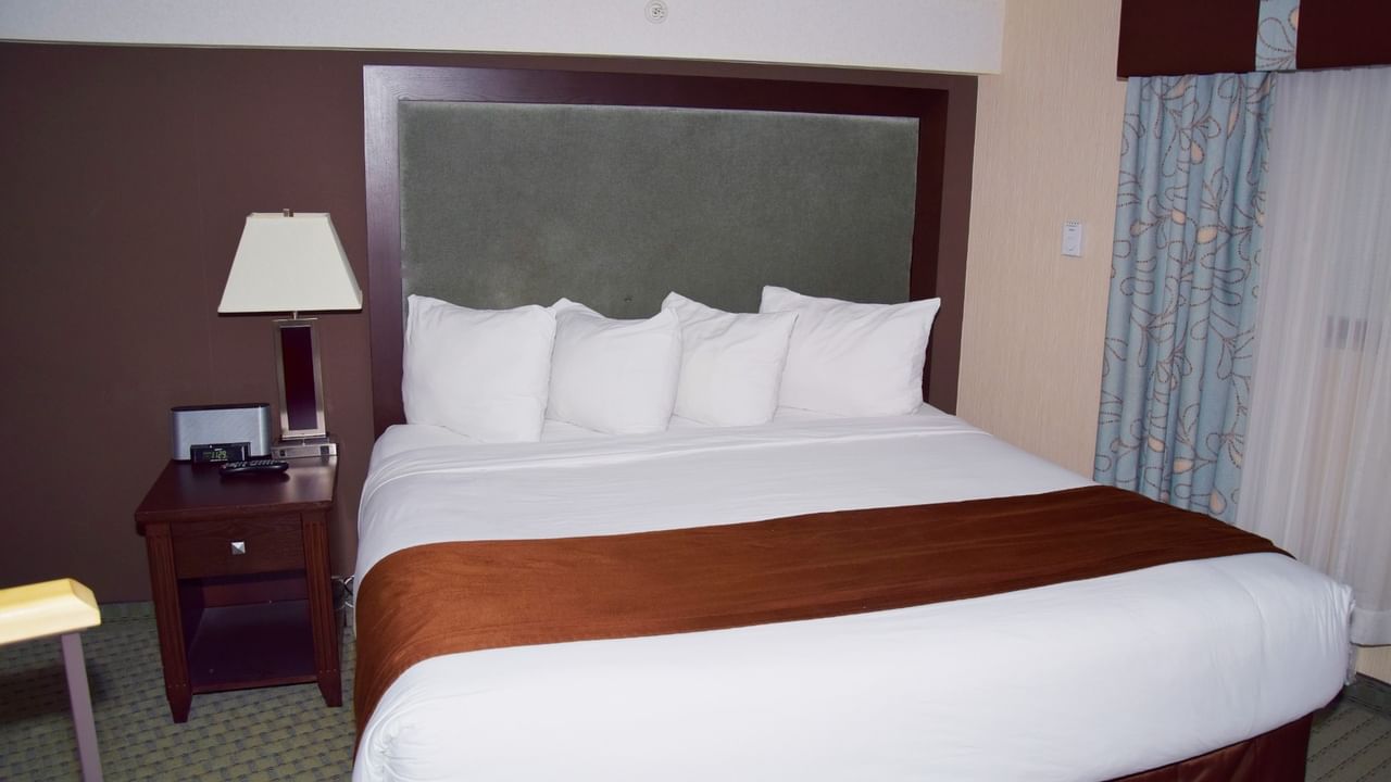A neatly made bed with white sheets, brown blanket, and pillows in a hotel room.