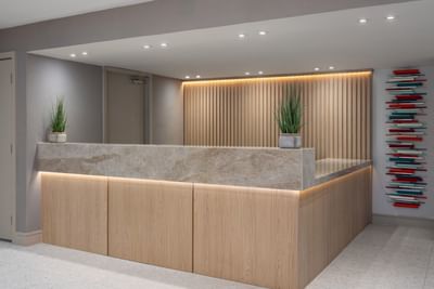 Modern hotel reception desk with a marble top, wood paneling, and cove lighting at The Harrison Hotel Downtown Hollywood