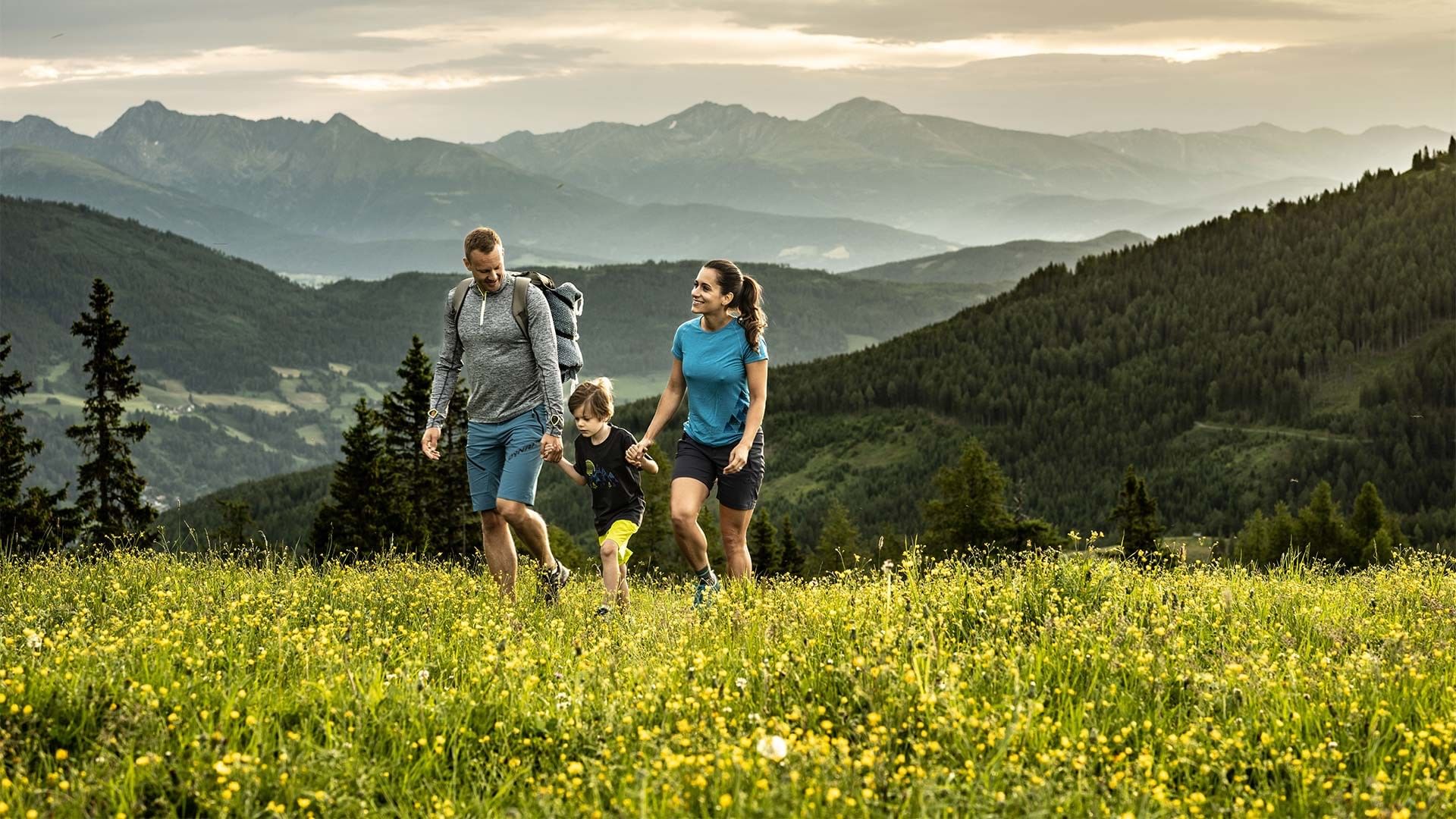 Familie wandert durch eine Blumenwiese in den Alpen mit Bergpanorama.