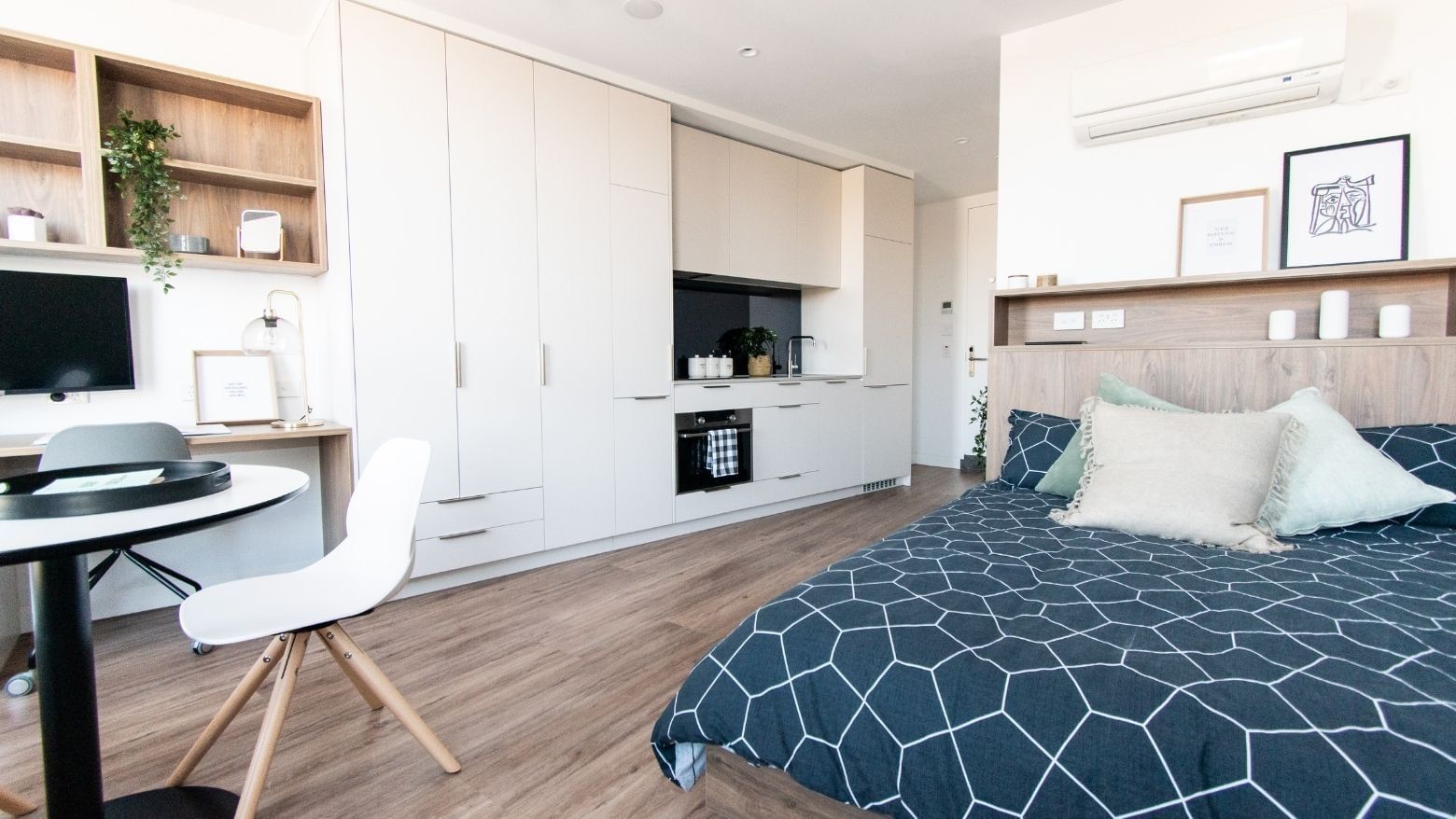 A modern, compact bedroom with a bed, desk, white cabinets, and wooden floors.