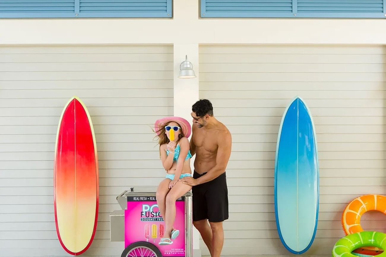 Two people by a popsicle cart between surfboards against a wall with shutters at The Grove Resort & Water Park