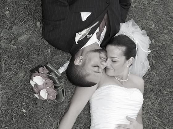 Black & white image of a wedding couple posing lying on the ground at Courtleigh Hotel & Suites