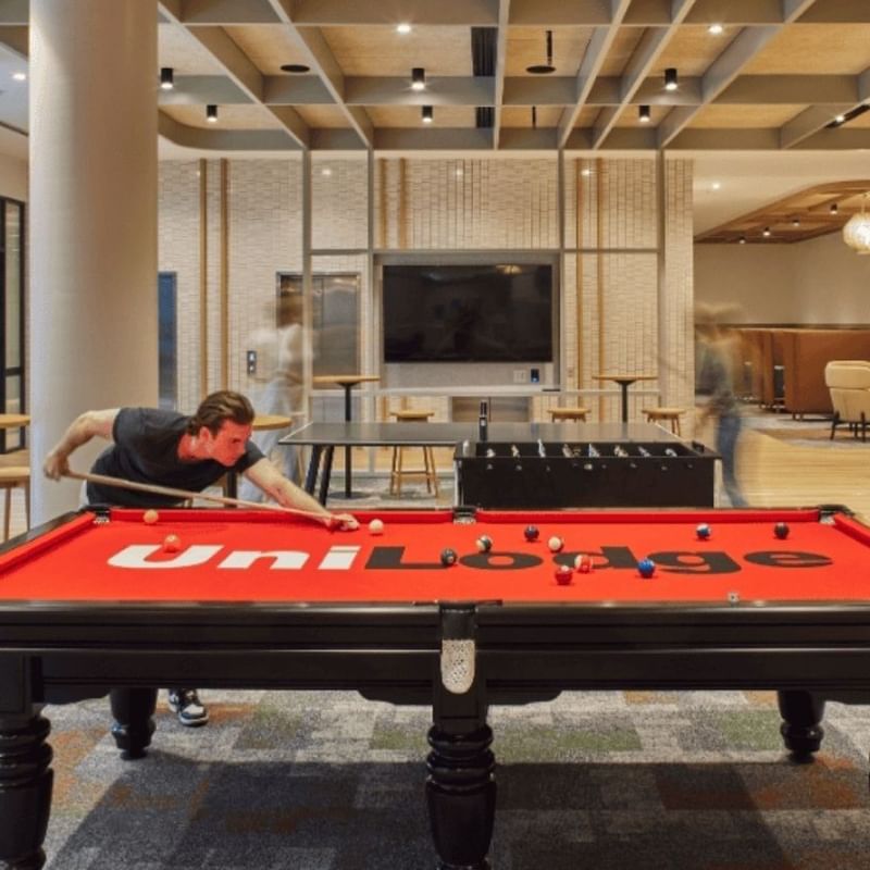 Man playing pool on a red UniLodge pool table in a bright, modern game room.