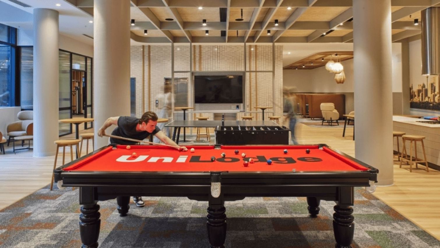 Man playing pool on a red UniLodge pool table in a bright, modern game room.