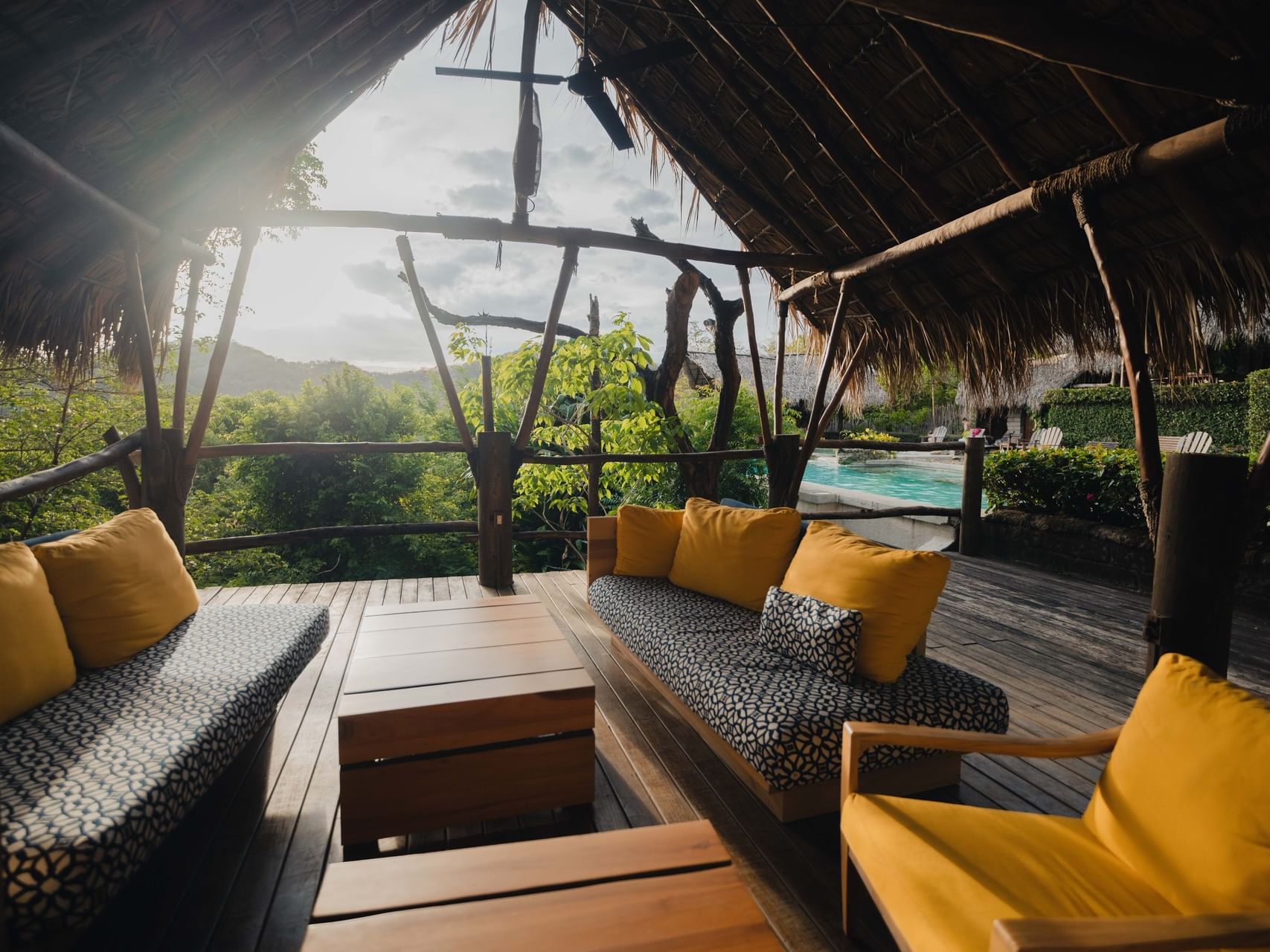 Yellow cushions on patterned sofas by wood tables under a thatched roof at Morgan's Rock Reserve & Ecolodge