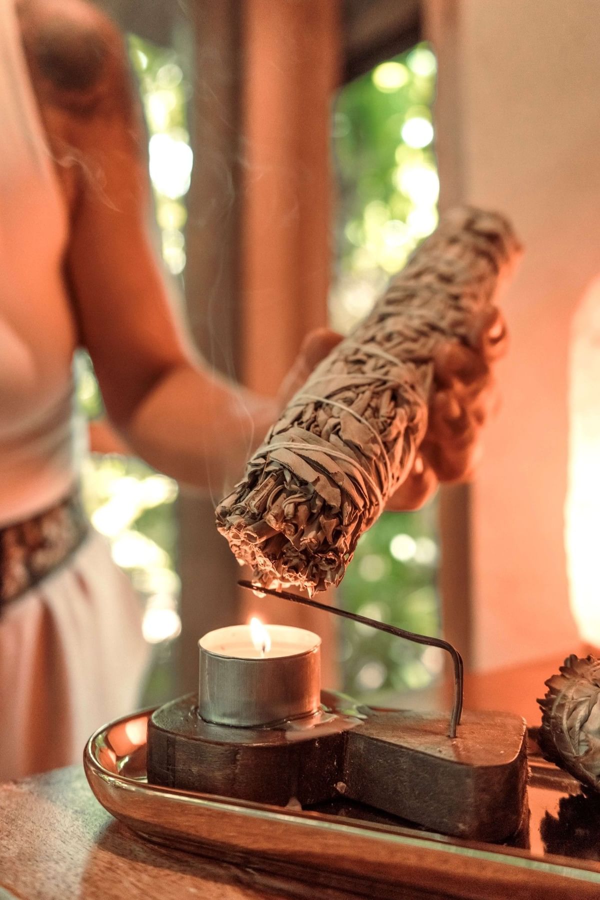 Hand holding a bundle of burning sage over a candle for a treatment in Lahari Wellness Center at Cala Luna Boutique Hotel