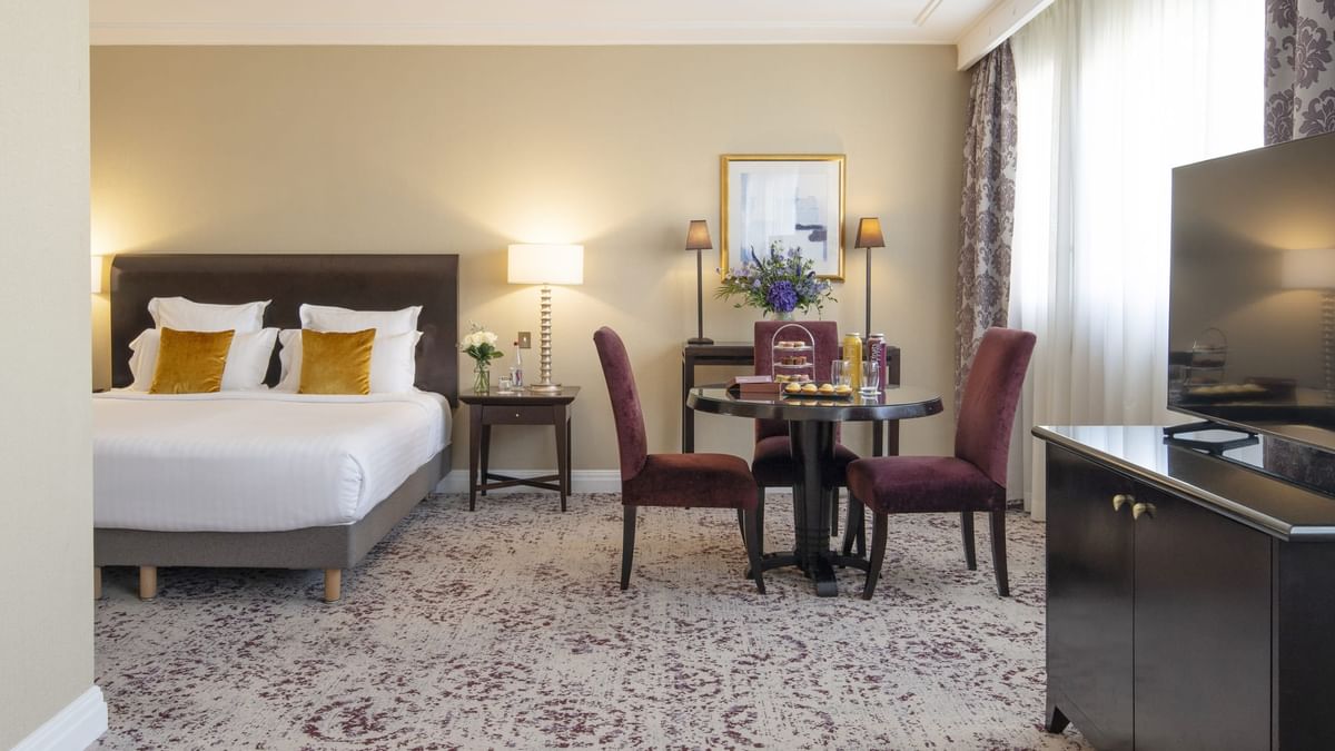 Junior Suite features a king bed by a small dining table with purple chairs at Warwick Paris Champs Elysées
