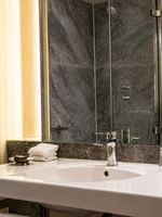 White sink by glass tumblers under a mirror near a white bathrobe hanging on the wall at Warwick Hotels & Resorts