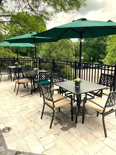 Outdoor patio area with black metal dining tables and chairs under green market umbrellas at The Simsbury Inn