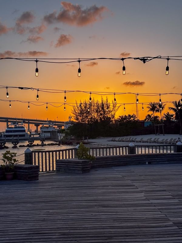 Glowing orange sunset by hanging string lights over a wooden deck at Warwick Paradise Island Bahamas