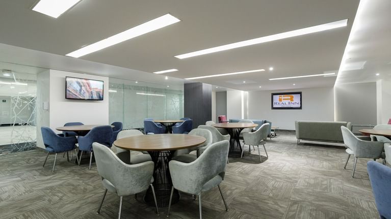 Executive meeting space with round tables and grey chairs, facing the logo on a TV screen at Real Inn Tijuana