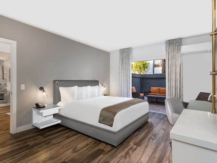 A modern hotel room with a large bed, wooden floor, and gray walls