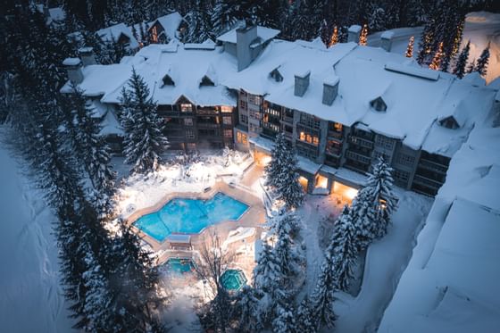 High angle view of snowy Blackcomb Springs Suites with illuminated pool