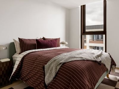 Modern bedroom with striped bedding and large window offering city views.