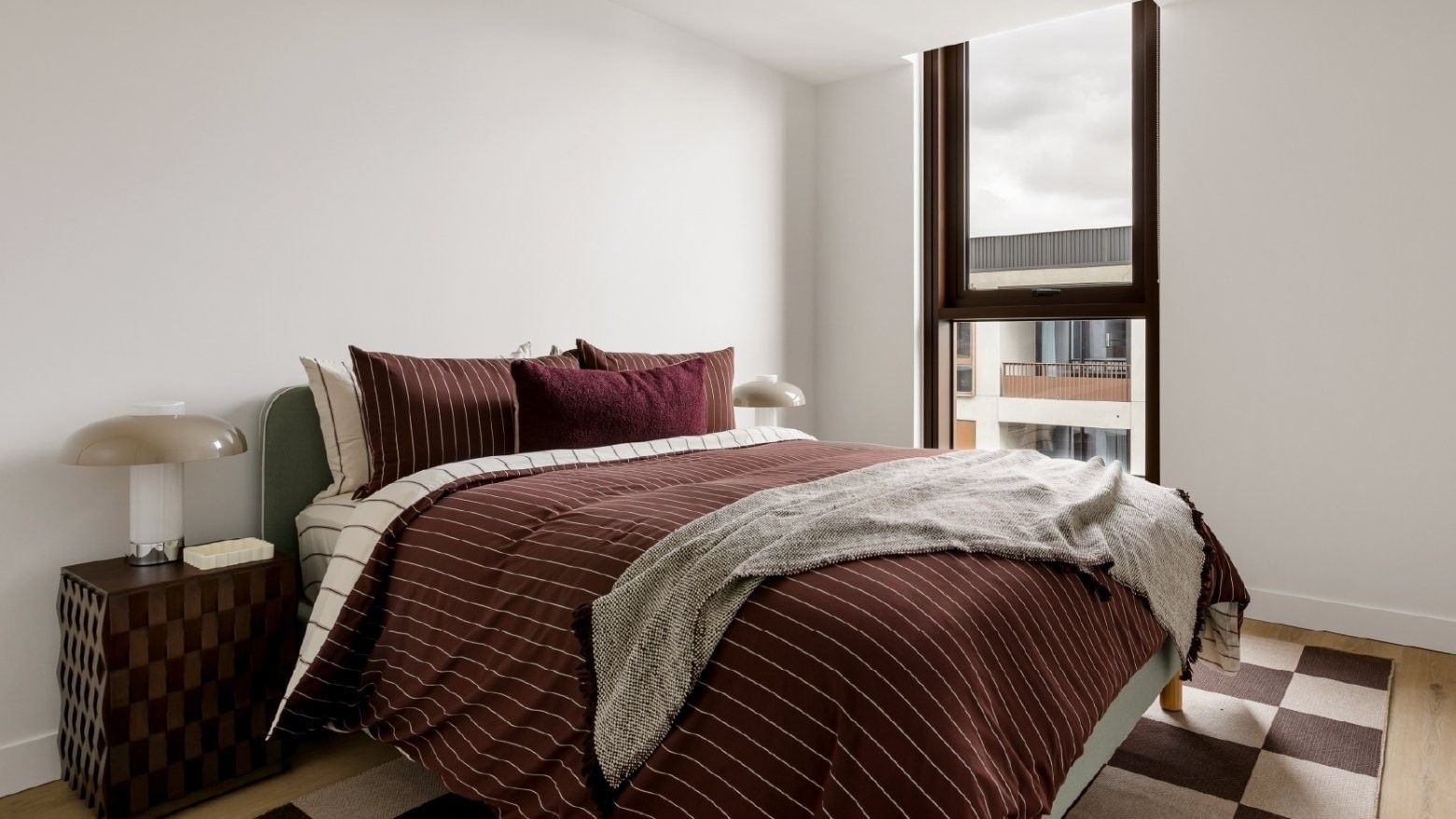 Modern bedroom with striped bedding and large window offering city views.