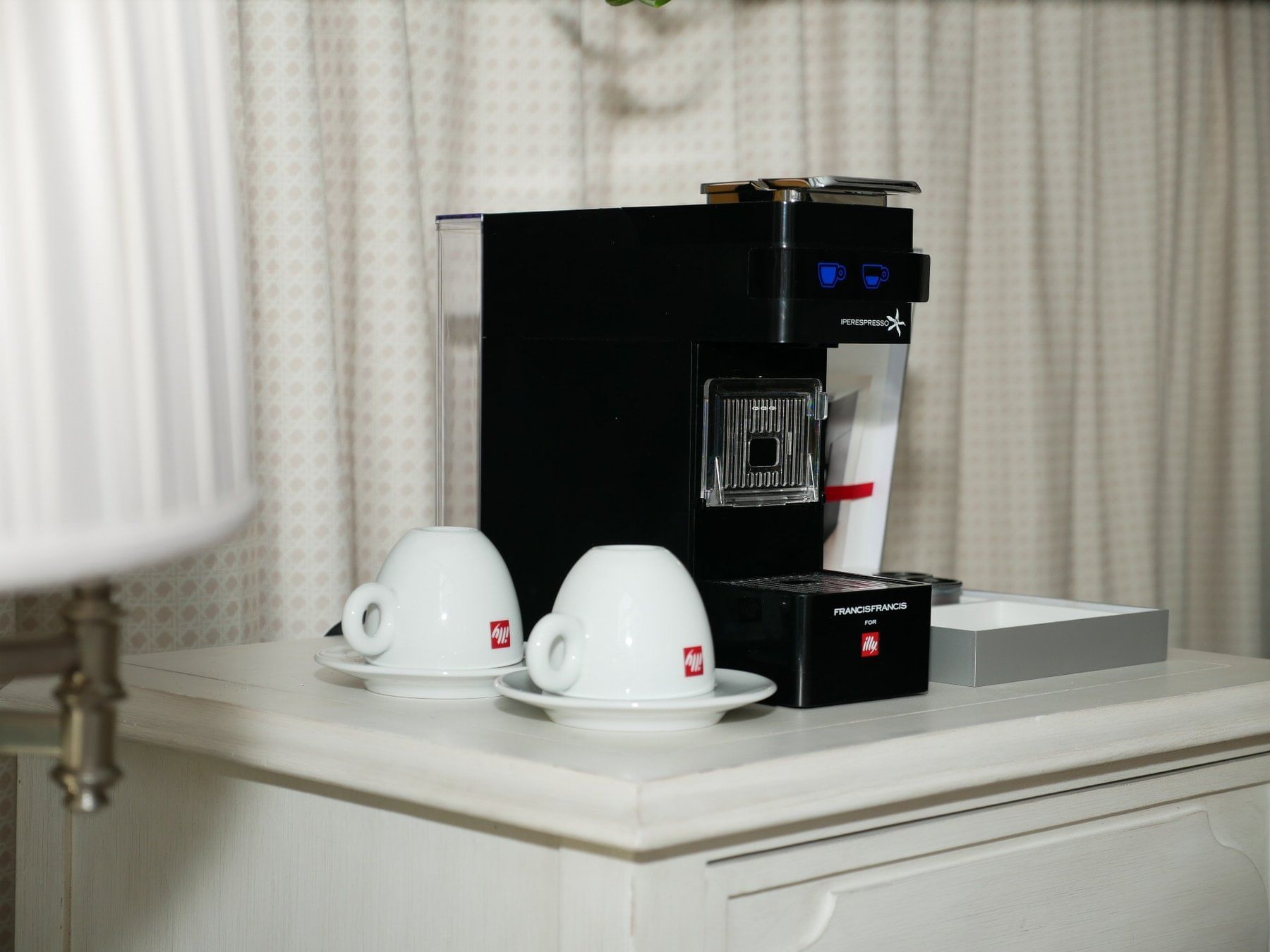A black coffee maker with two white cups on a white cabinet