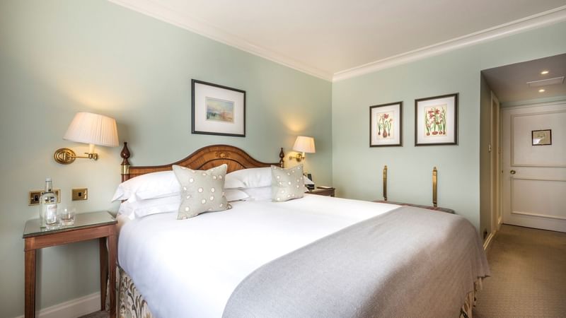 Elegant bedroom with large bed, bedside lamps, framed artwork, and a side table with a bottle and glass.