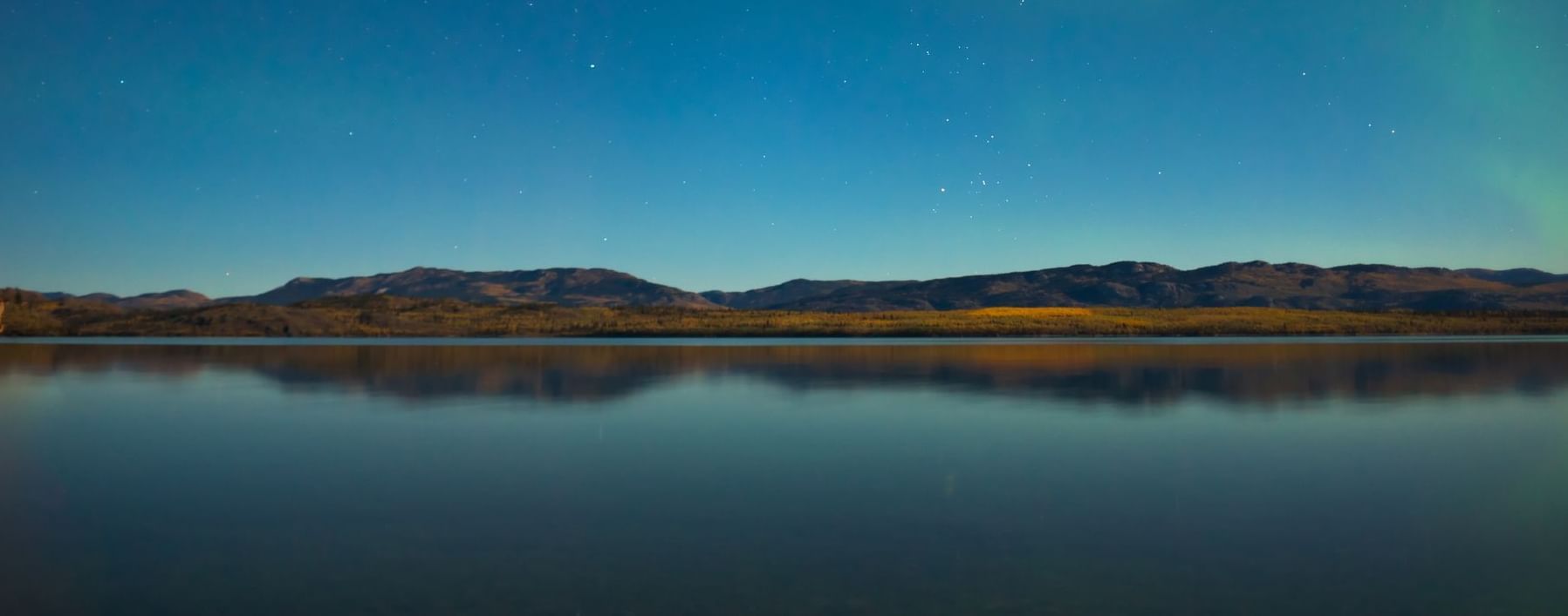 Lake surrounded by mountains with starry evening sky above