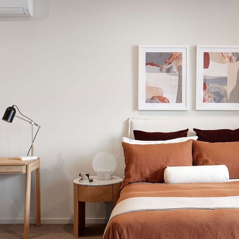 Cozy bedroom in Melbourne with brown bedding, a desk, a chair, two nightstands, and two framed pictures on the wall.