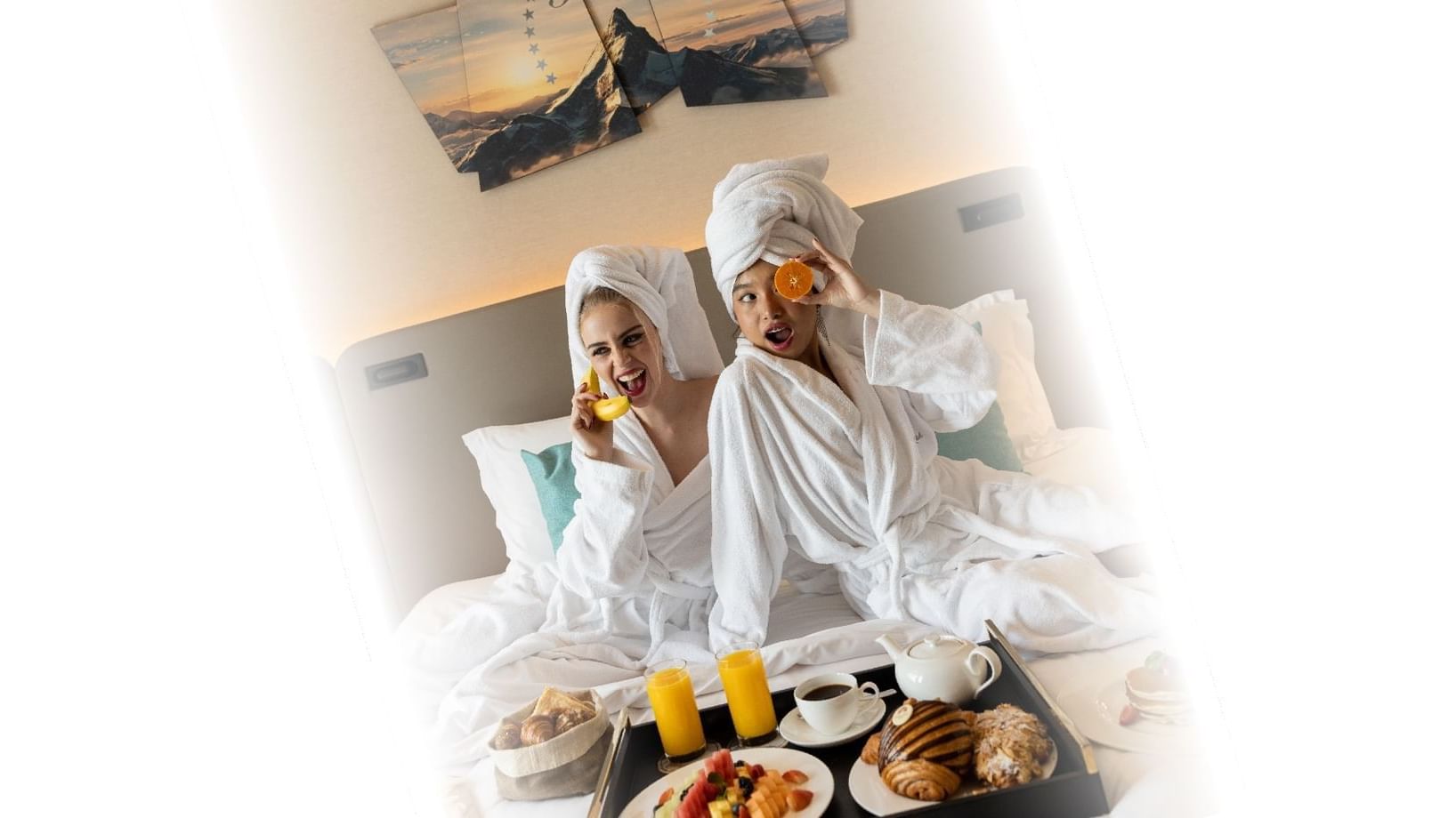 Two playful women in bathrobes with fruit and breakfast in a plush bedroom suite at the Paramount Hotel Dubai
