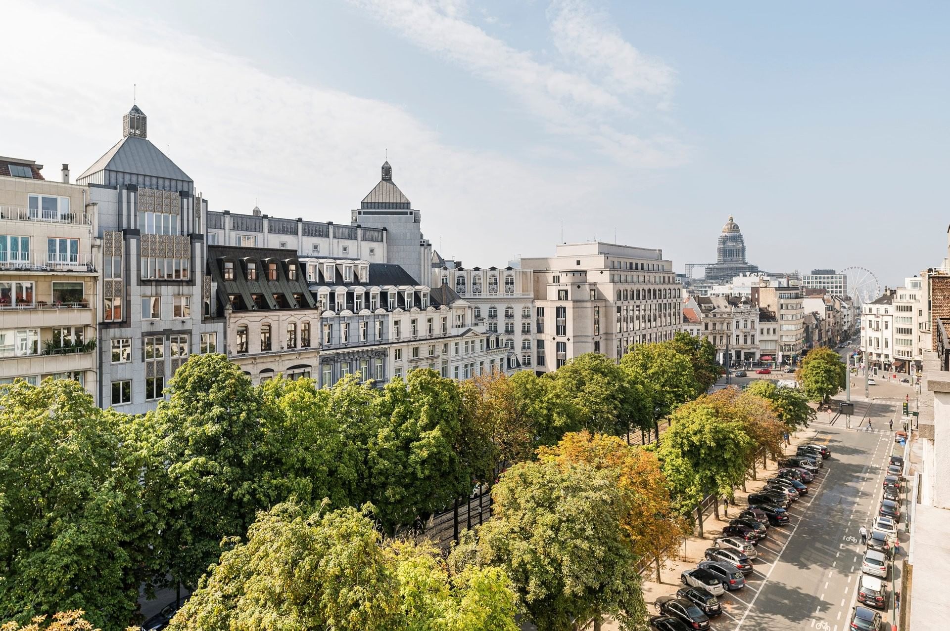 High-angle view of city buildings by a row of green trees under a pale sky near Hotel Barsey by Warwick