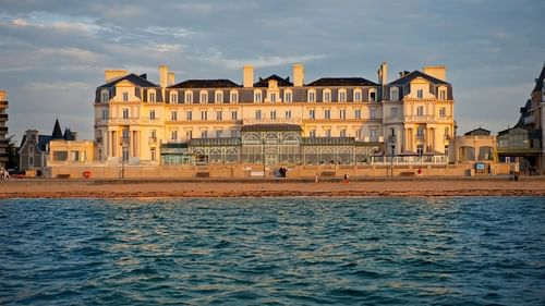 Panoramic exterior view of Le Grand Hôtel des Thermes & the Sea with classic architecture by a sandy beach at sunset