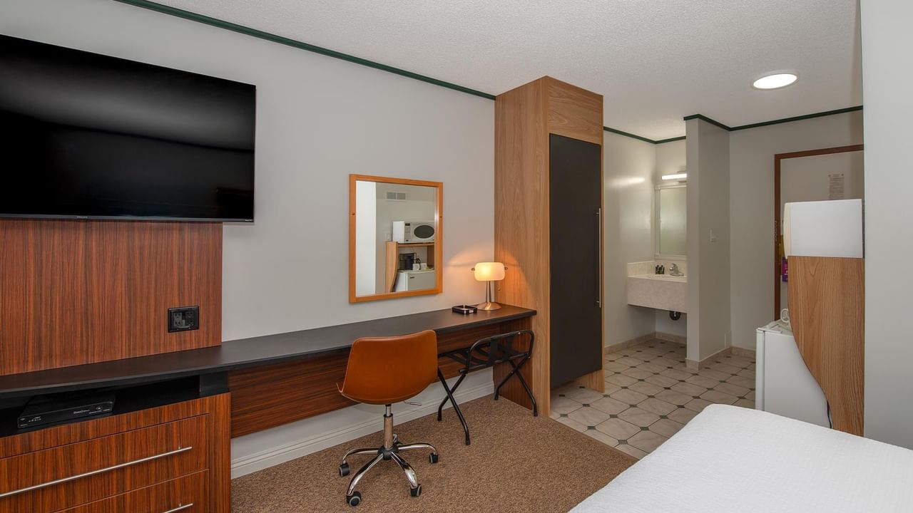 room workspace with desk, chair, TV and partial view of the bed at Coast Whitecourt Hotel
