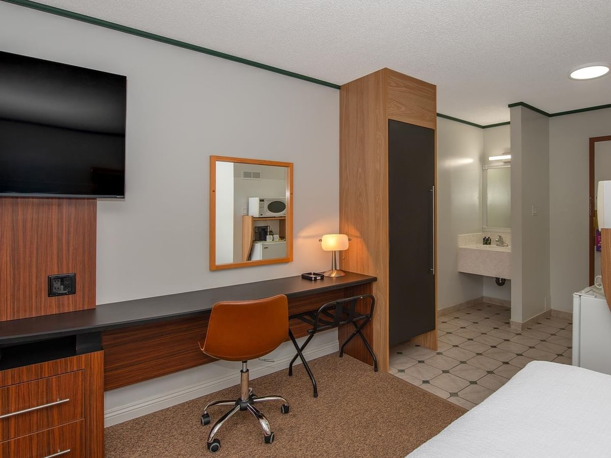 Guest room with a wall-mounted TV, work desk, chair and partial view of the bed