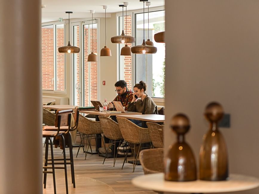 Deux personnes travaillant ensemble à une table dans le salon de l'Hôtel Rivella.