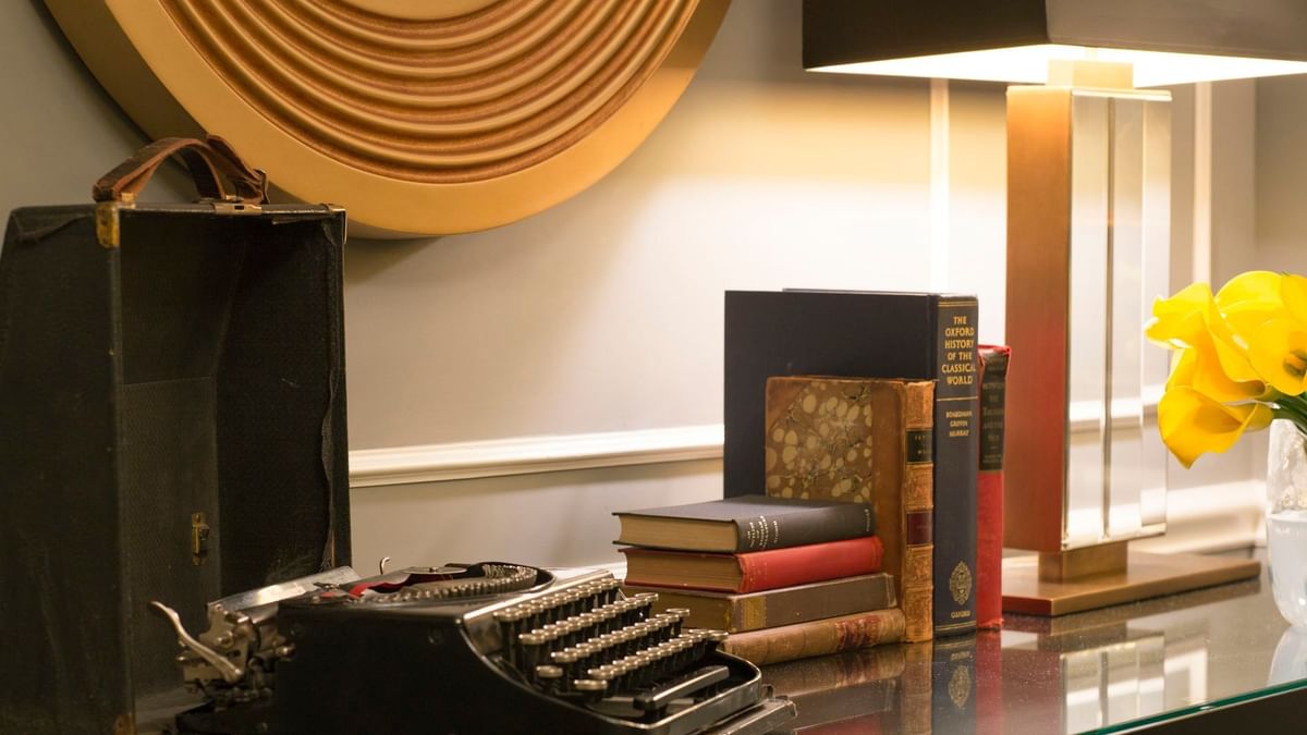 Vintage black typewriter in case beside stack of old books on a glass console table in Randolph Suite at Warwick New York