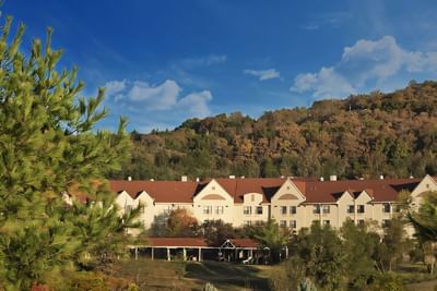 Multi-story Branson Hillside Hotel with a red roof nestled against a backdrop of dense, wooded hills
