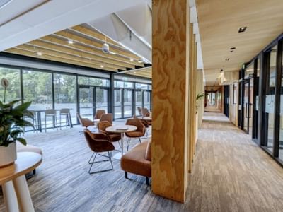 Modern hotel lobby with wooden accents, terracotta seating, floor-to-ceiling windows, and a bright corridor at Tupuārangi.