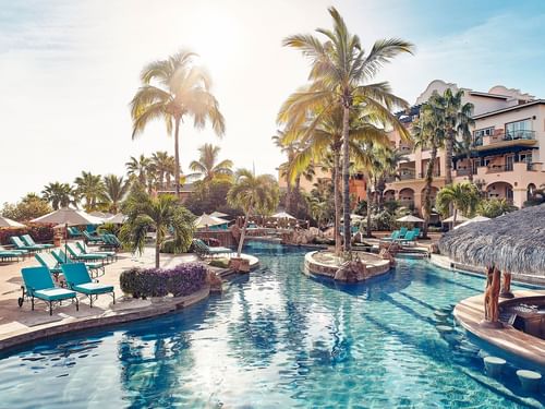 Delfines Bar pool with lounge chairs, a swim-up bar, and palm trees at Hacienda del Mar Los Cabos.