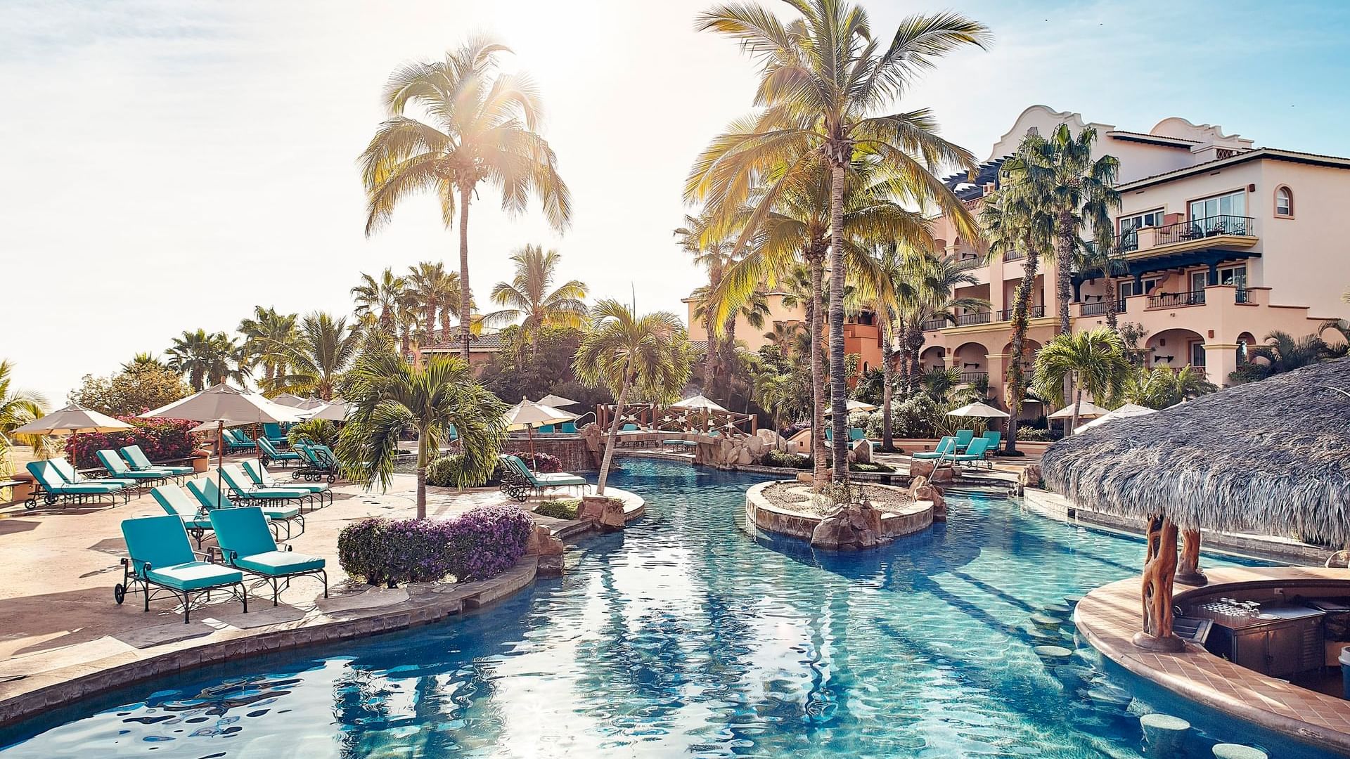 Delfines Bar pool with lounge chairs, a swim-up bar, and palm trees at Hacienda del Mar Los Cabos.