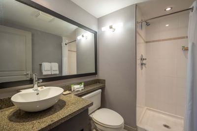 Bathroom with a sink, mirror, toilet and shower with white curtain in Jacuzzi Suite at Sandman Hotel & Suites Winnipeg Airport