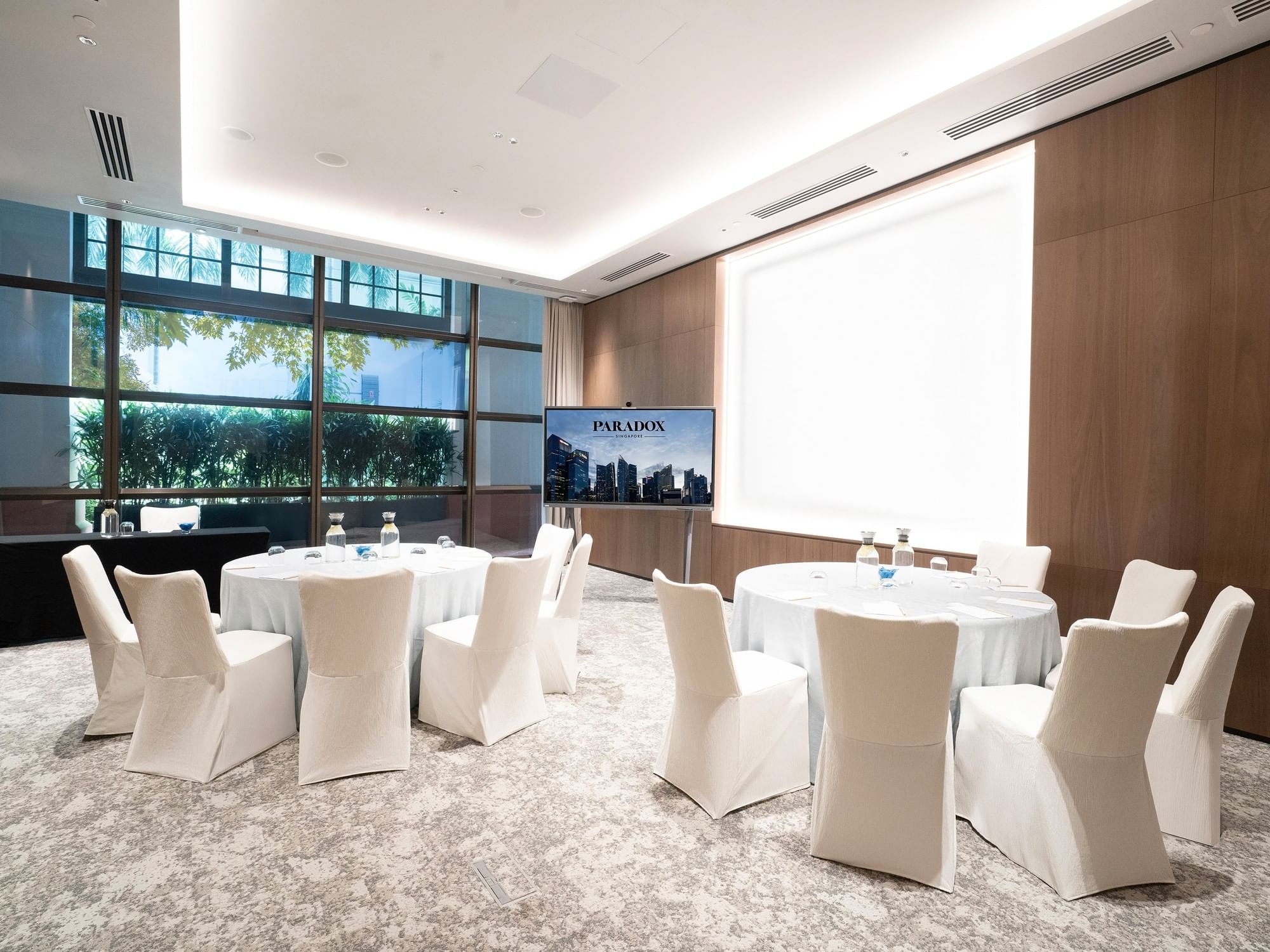 Cluster setup in a meeting room at Paradox Singapore, featuring small groups of tables and chairs arranged for breakout discussions in a contemporary, professional setting.