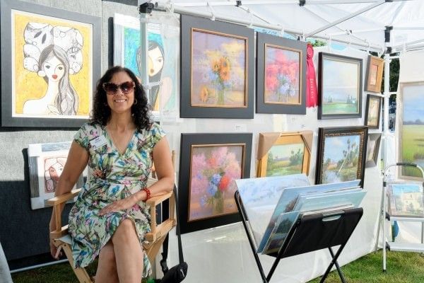 A woman sits in a tent filled with artwork at the Winter Park Autumn Art Show, a fall festival in Orlando.
