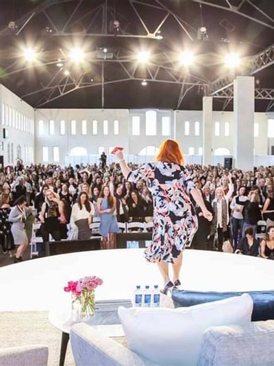 Woman presenting to an audience in a large, well-lit conference hall at Sofitel Brisbane Central