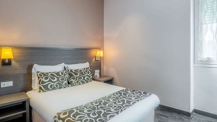 A cozy bed with pillows & a nigh lamp at The Originals Hotels