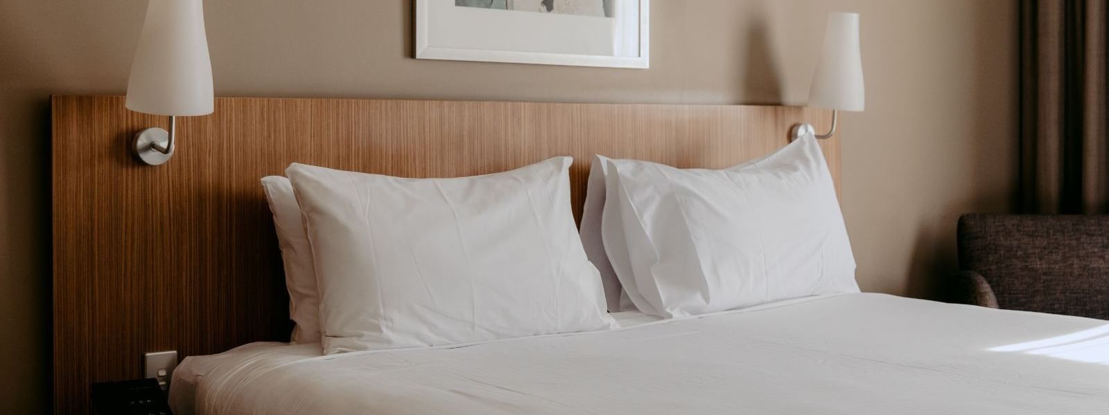 A hotel room with a neatly made bed, two white pillows, and framed artwork above it.