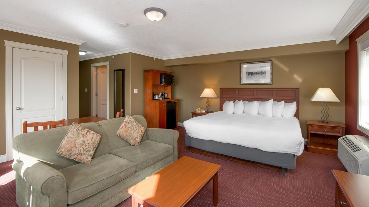 Spacious hotel room with king bed, gray sofa, wooden furniture, and warm earth-toned walls at Coast Edson Hotel.