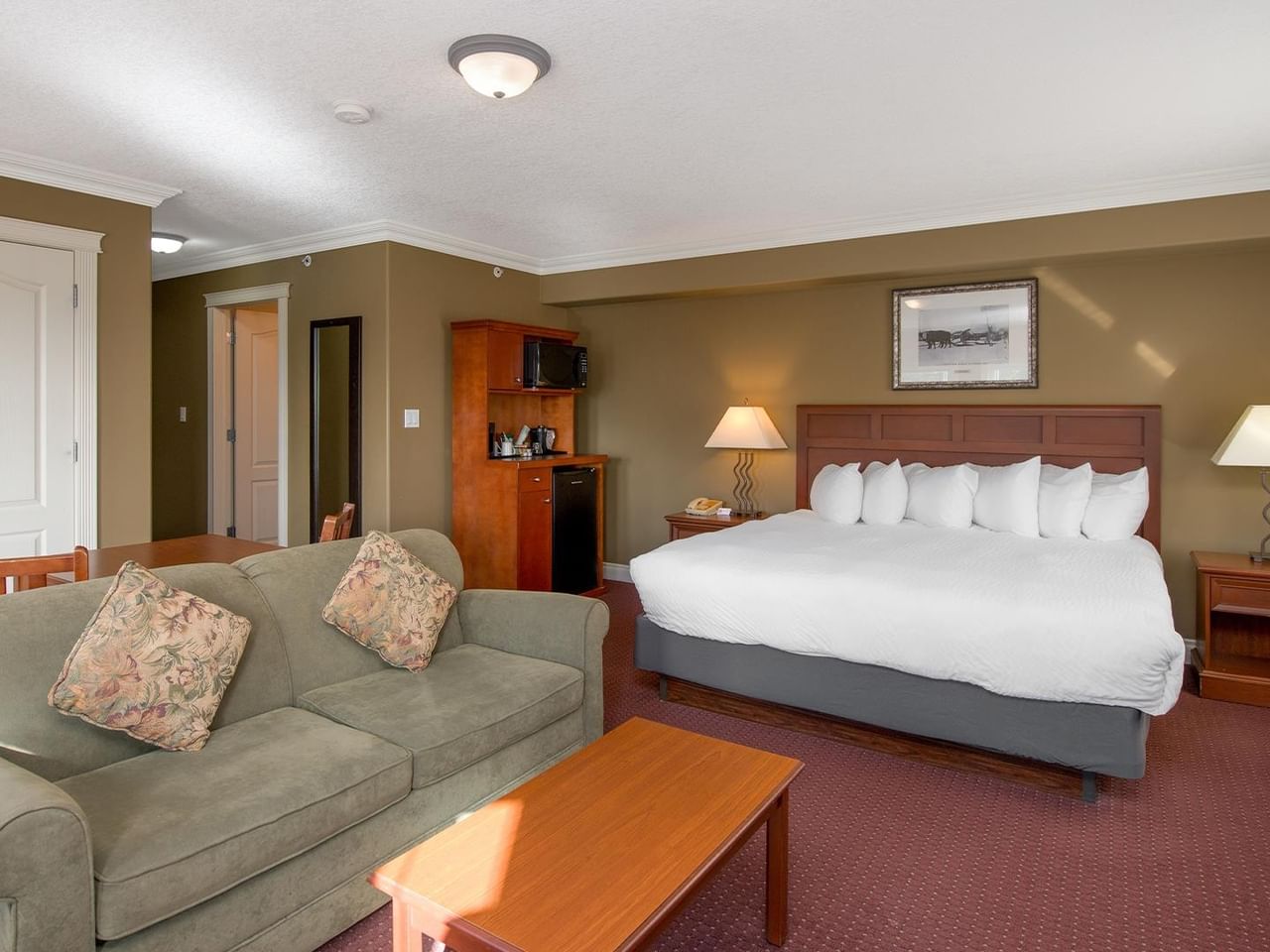 Spacious hotel room with king bed, gray sofa, wooden furniture, and warm earth-toned walls at Coast Edson Hotel.