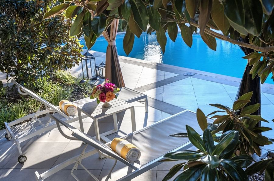 Lounge chairs by a pool under green leaves surrounding a sunlit patio area at Warwick Melrose Dallas
