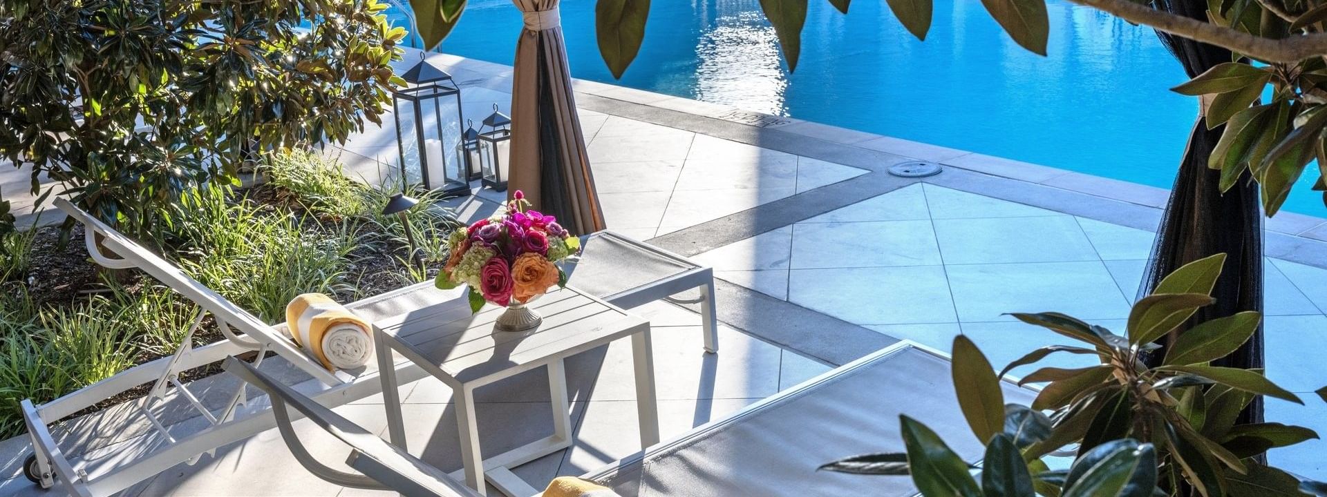 Lounge chairs by a pool under green leaves surrounding a sunlit patio area at Warwick Melrose Dallas