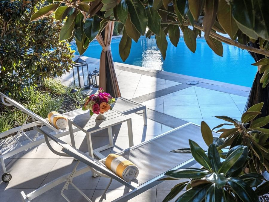 Lounge chairs by a pool under green leaves surrounding a sunlit patio area at Warwick Melrose Dallas