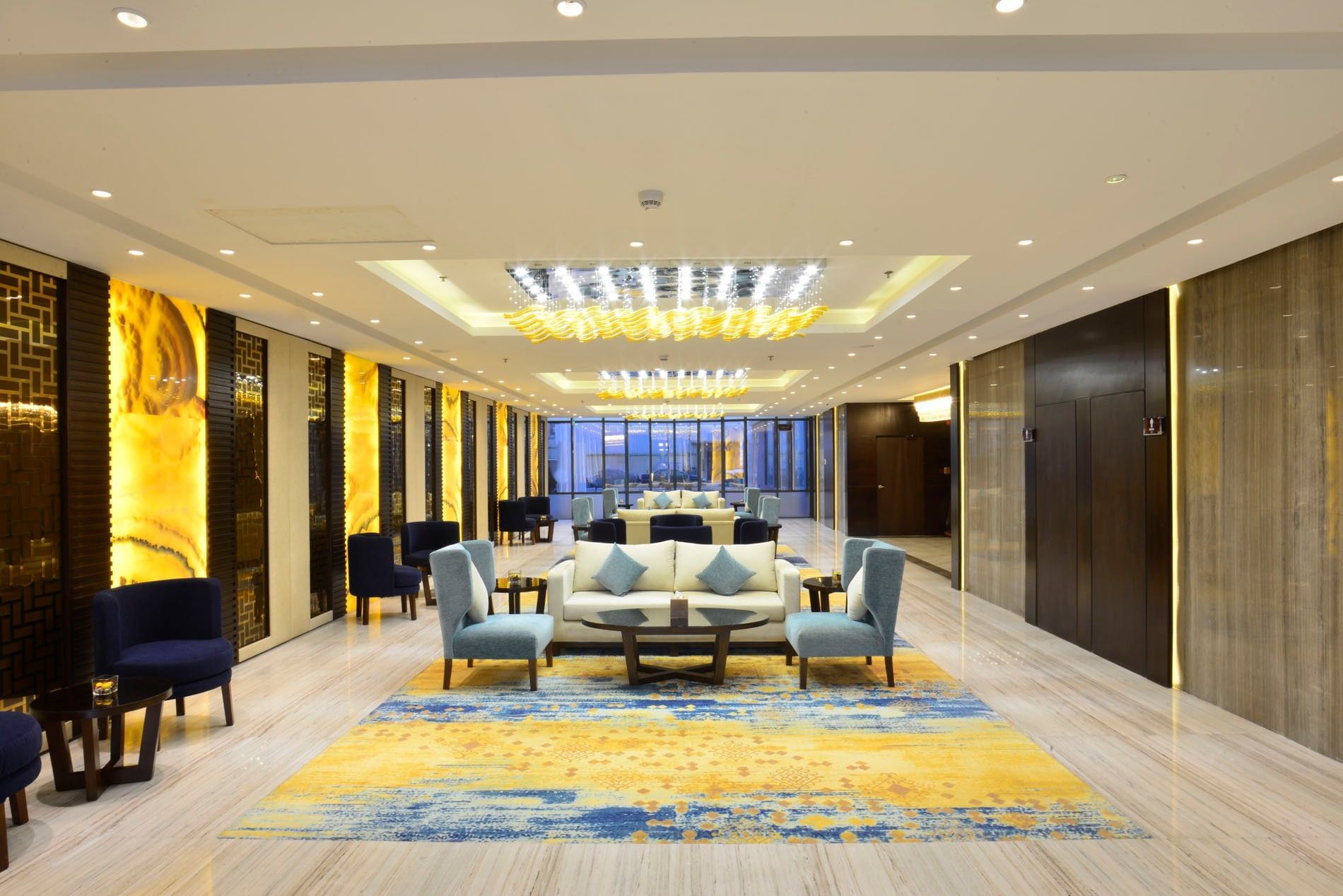 Plush sofas by glass tables under gold chandeliers in the lobby lounge at Naviti By Warwick Dammam