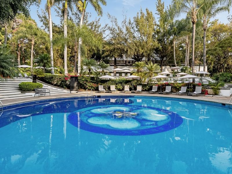 Luxurious swimming pool surrounded by lounge chairs and lush greenery at Grand Fiesta Americana