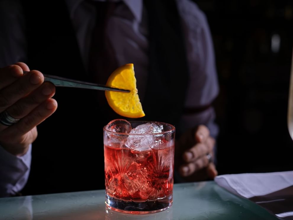 Bartender placing a slice of orange by a glass of red cocktail in Capital Bar at The Capital Hotel, Apartments and Townhouse